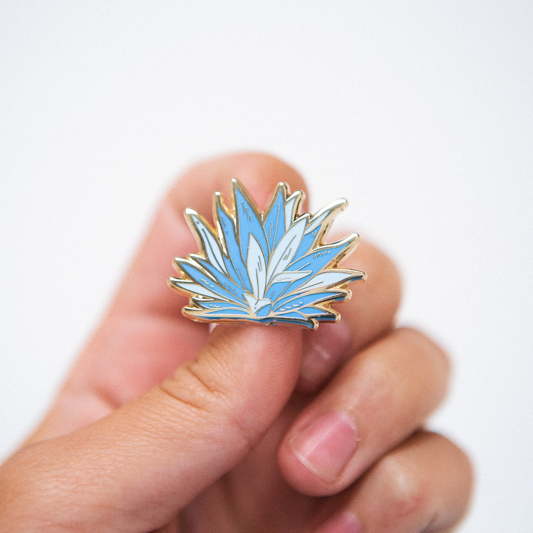 a hard enamel pin of a Blue Agave plant in blue color with gold metal plating