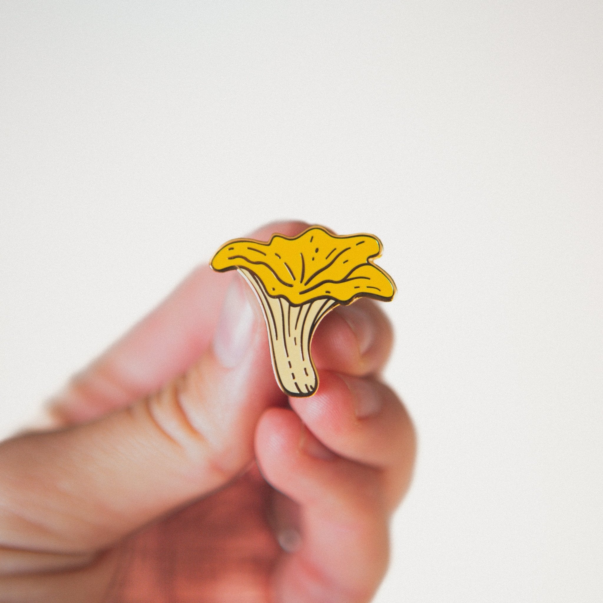 a hard enamel pin of an orange chanterelle mushroom. A cute nature plant pin that will accessorize a backpack, tote, lapel, hat, or jacket
