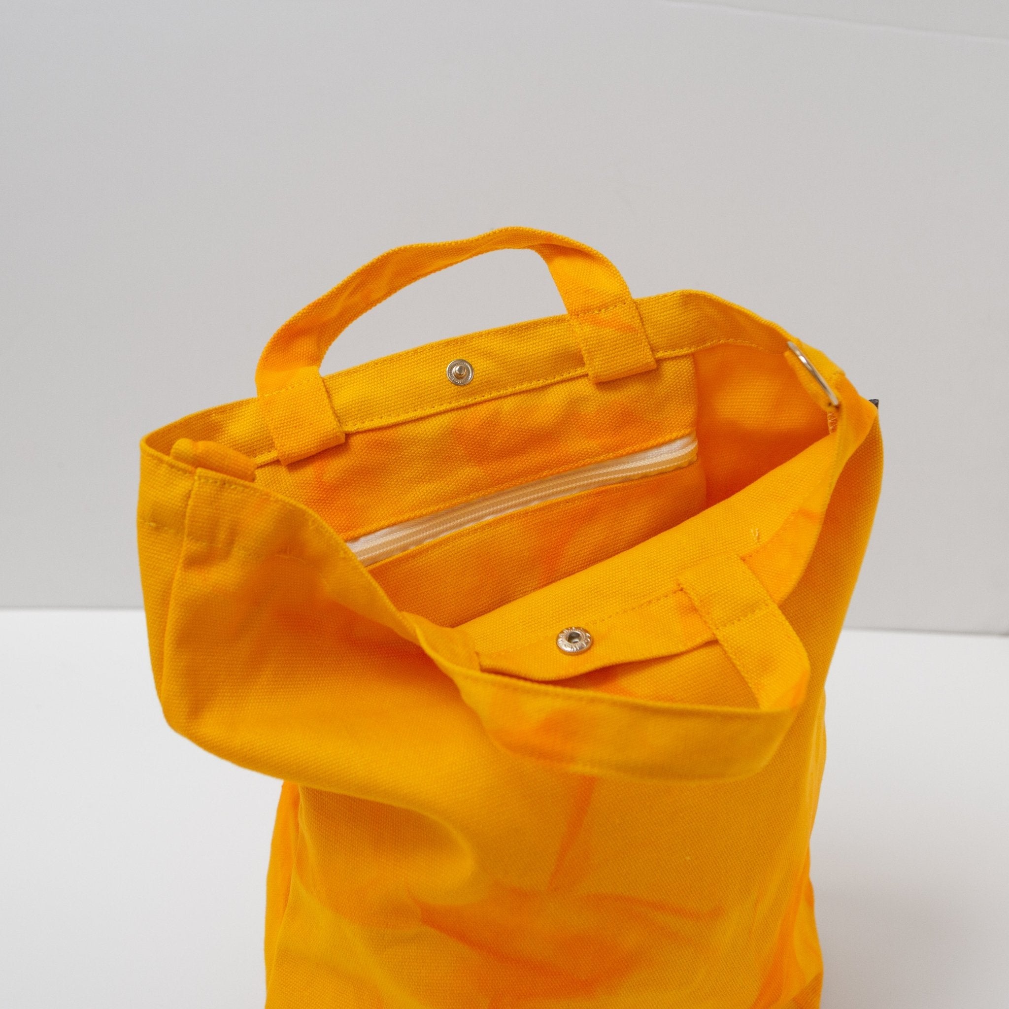 a tie dyed canvas tote in a bright yellow color with orange dye