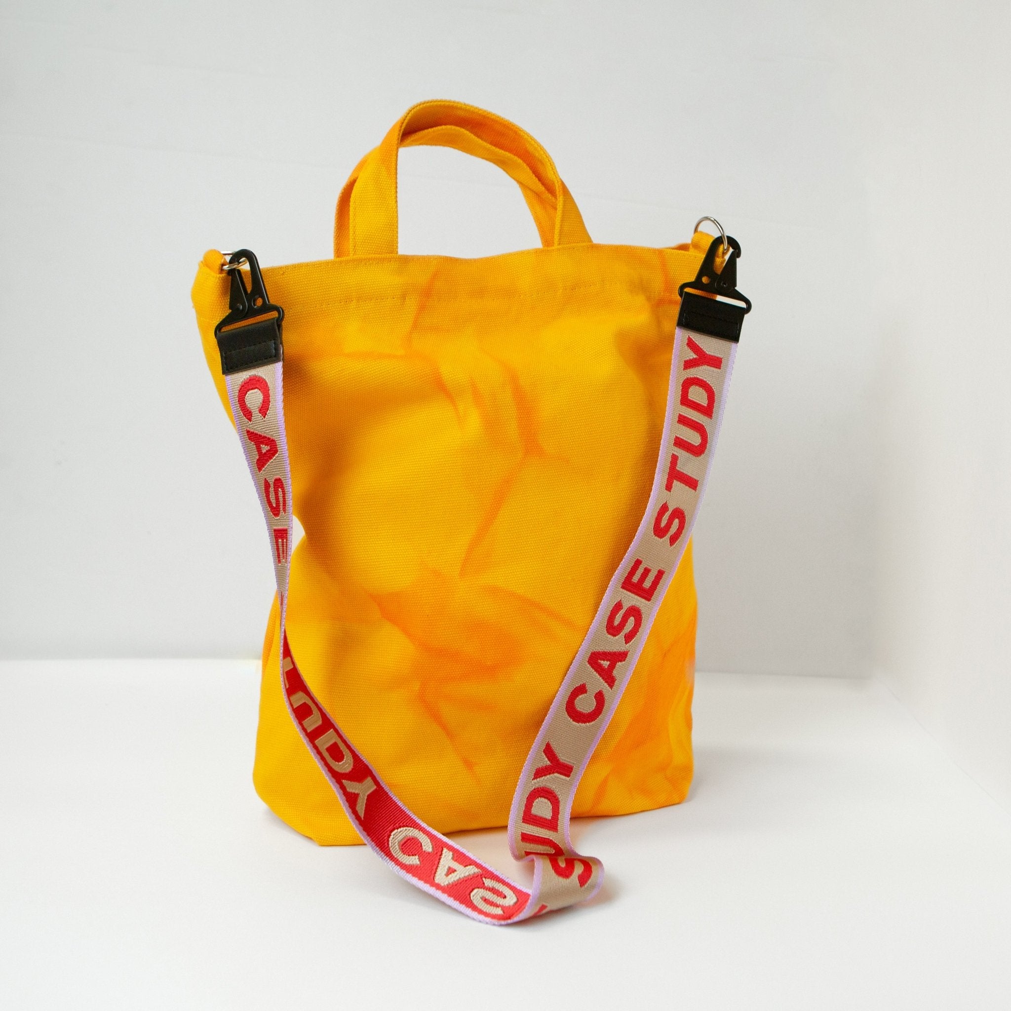 a tie dyed canvas tote in a bright yellow color with orange dye and a red and lavender  crossbody strap