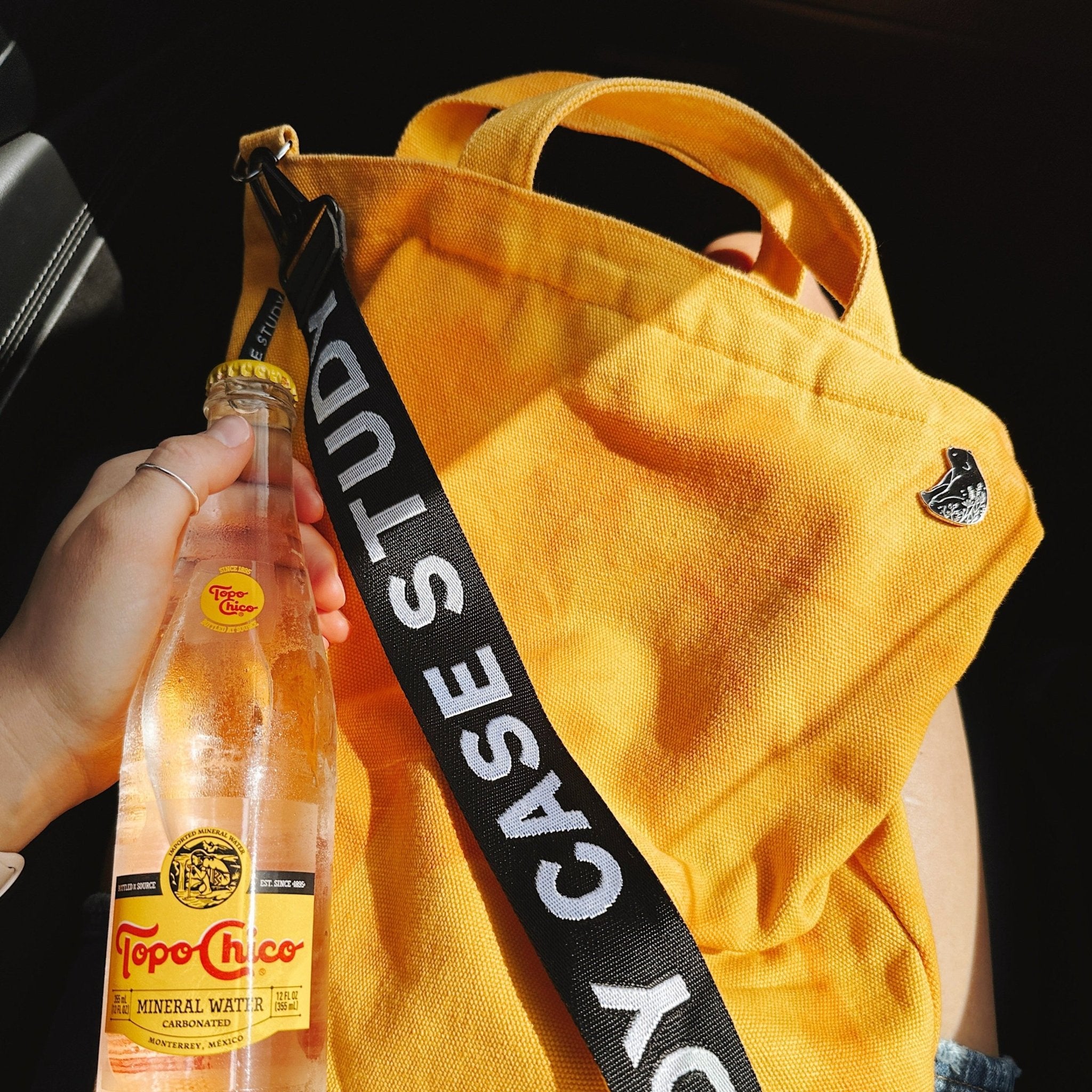 a tie dyed canvas tote in a bright yellow color with orange dye and a black and white crossbody strap