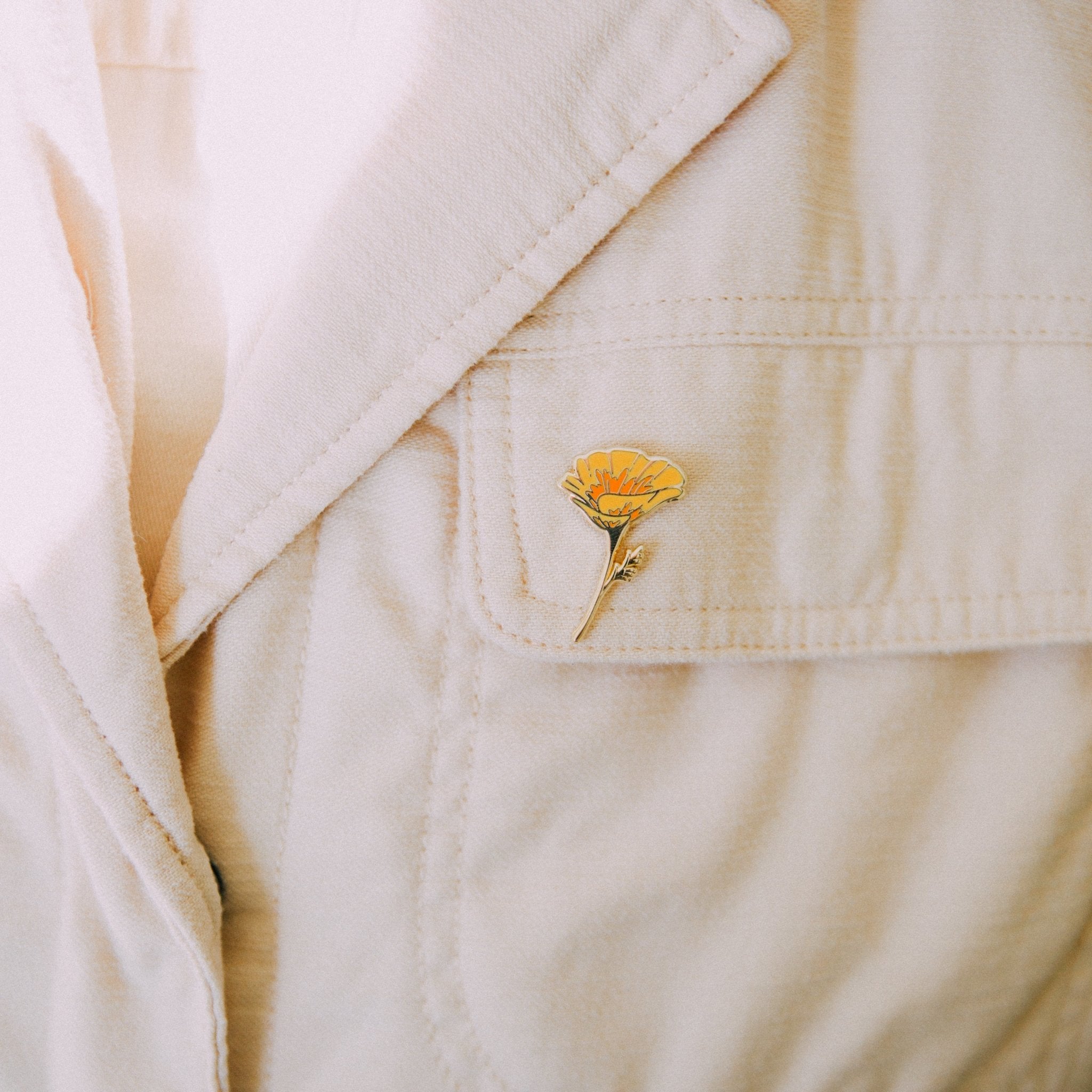 a hard enamel pin of an orange california poppy wildflower made from hard enamel and gold metal plating. a cute plant wildflower pin for backpacks, totes, hats, lapels, and jackets