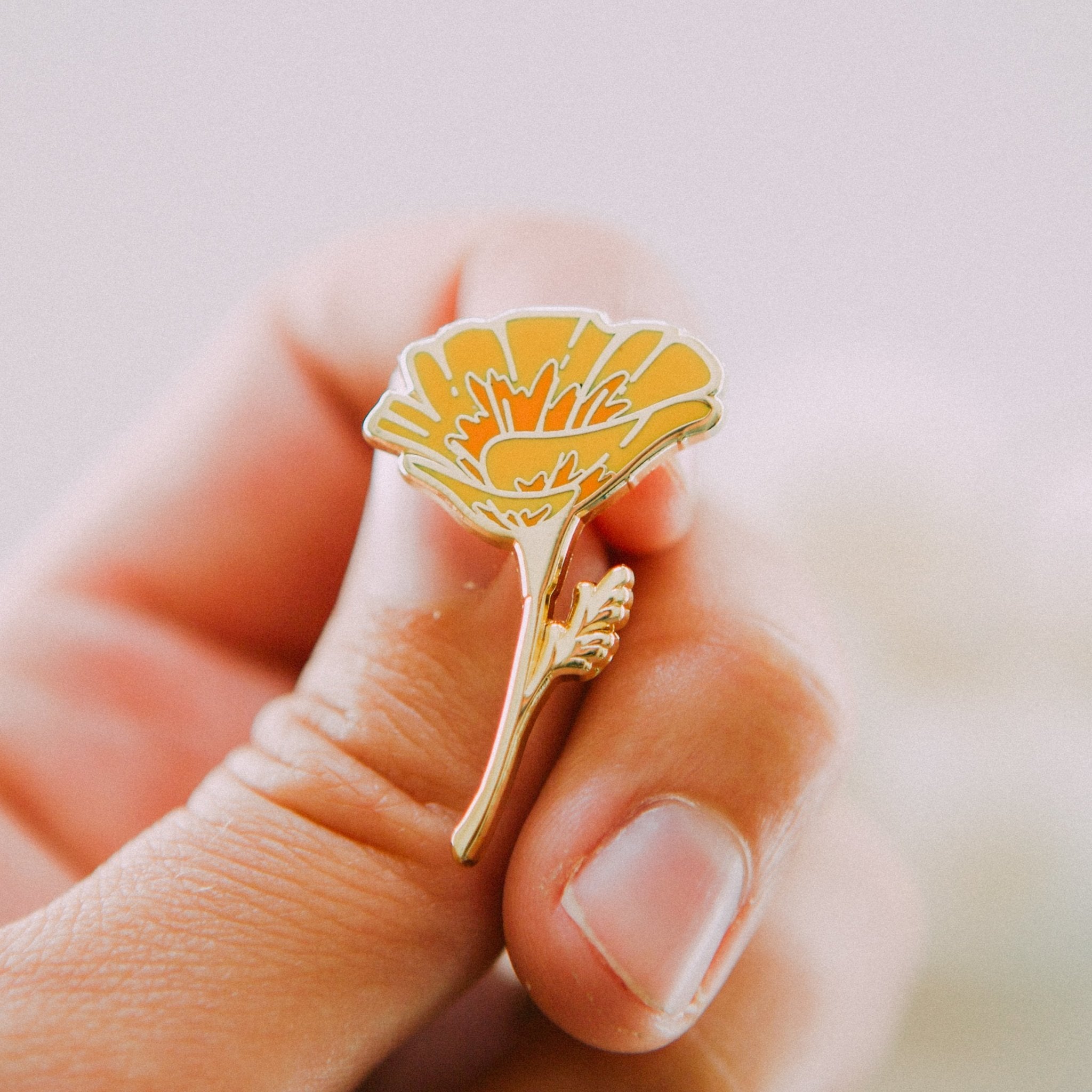 a hard enamel pin of an orange california poppy wildflower made from hard enamel and gold metal plating. a cute plant wildflower pin for backpacks, totes, hats, lapels, and jackets