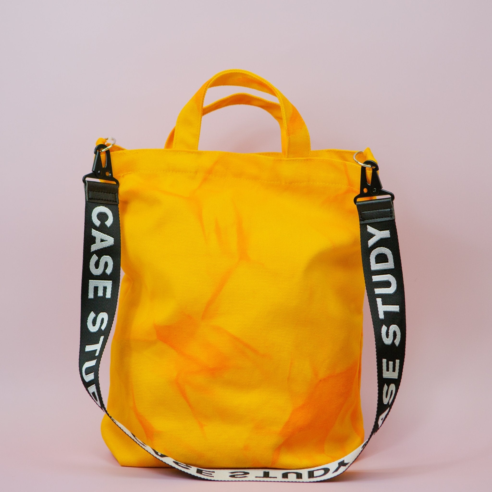 a tie dyed canvas tote in a bright yellow color with orange dye and a black and white crossbody strap