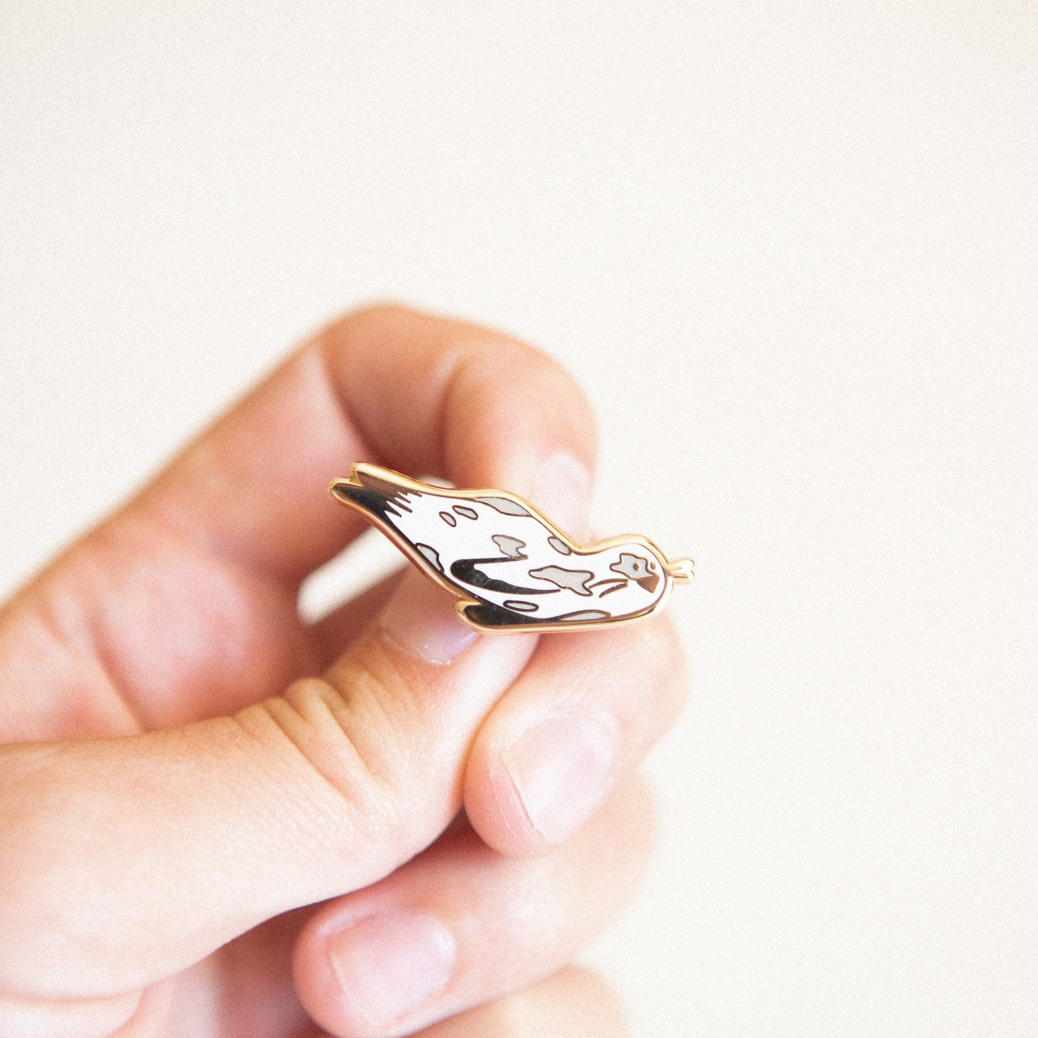 a cute animal hard enamel pin of a harbor seal swimming through the ocean. Made with white enamel and gold metal plating